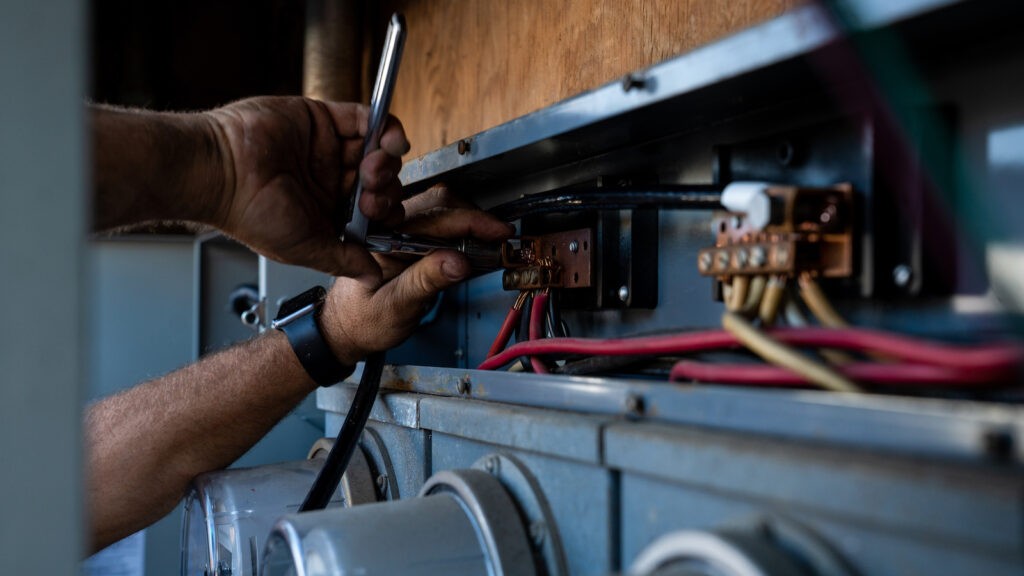 An electrician with his hands above the submeters inspecting the wires.