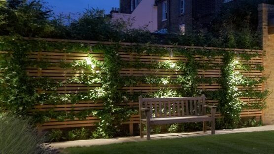 Lights installed on the fence of a house that help light up the bench that is placed along the wall.