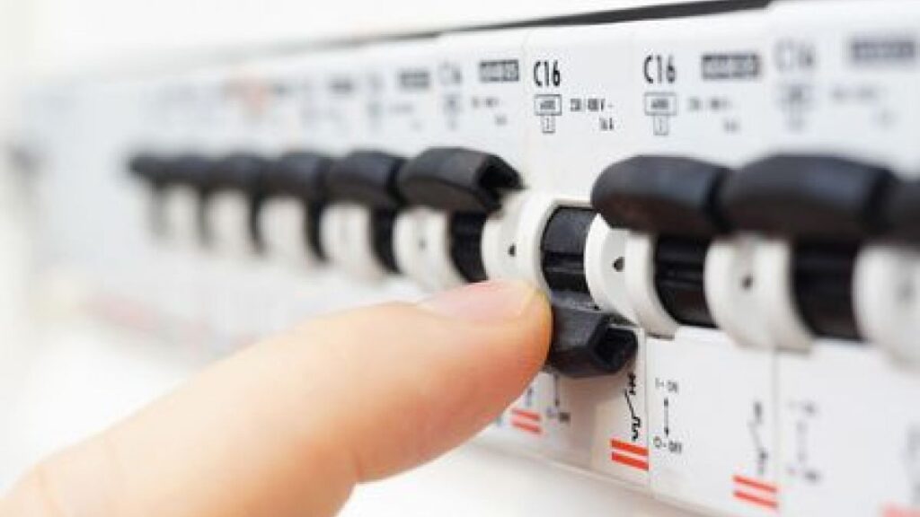 Residential electrician flicking a fuse box switch. 