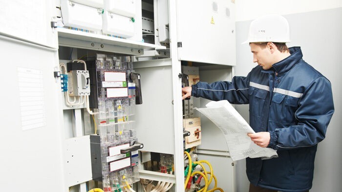 A commercial electrician at work inspecting cabling connection of electrical switch gears in industrial building.