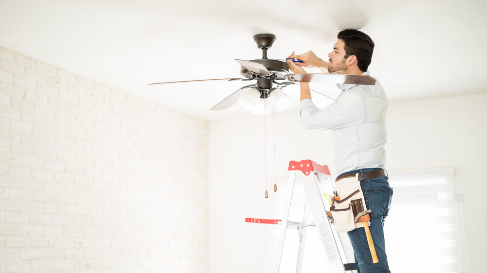 Electrical contractor on a ladder inspecting the electrical wires of a living room fan.