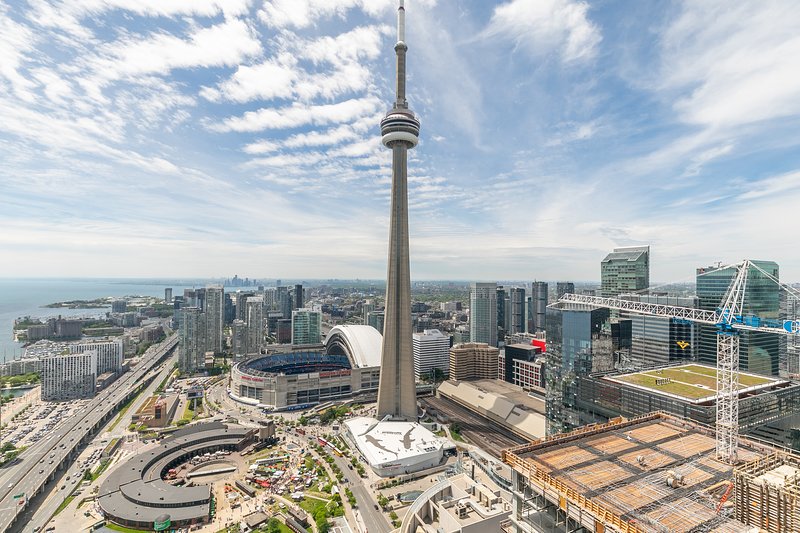 The Toronto Skyline with the CN Tower on a sunny summer day.  A construction crane, the rogers centre stadium, and many condo towers.