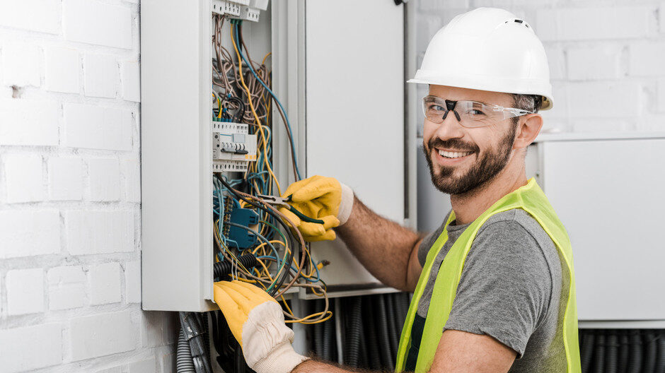 Man with hardhat and safety vest inspecting the electrical panel board in a residential home. 