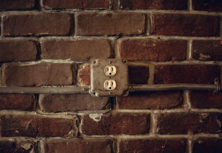 An old, worn bargain receptacle in a metal box on a brick wall
