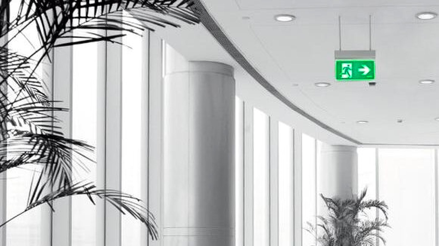 Green running man exit sign hanging in a bright office corridor